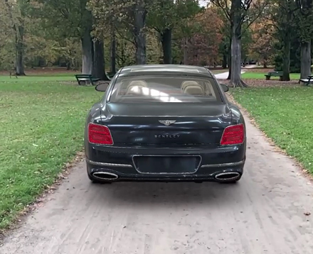 Auf einem Weg in einem Park steht ein 3D Model eines Bentley Flying Spur Auto, man erkennt sein Heck sehr deutlich. 