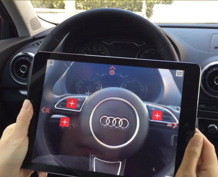 2 Hände halten ein iPAD seitlich und die Kamera ist an und zeigt das Lenkrad eines Audi. Im Kamerabild sind zusätzlich kleine AR Informations-Hotspots auf das Lenkrad augmentiert. 